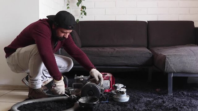Handyman kneeling on rug repairing broken vacuum cleaner with screwdriver at home