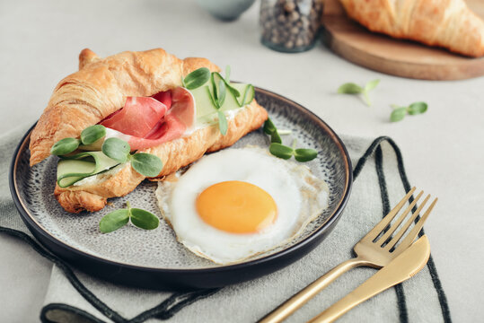 Croissant sandwich with cream cheese, cucumber and ham, served with a fried egg