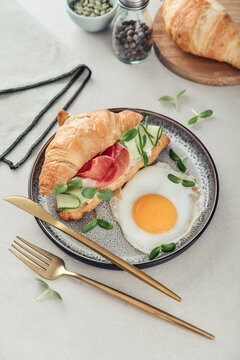 Croissant sandwich with cream cheese, cucumber and ham, served with a fried egg
