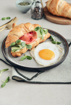 Croissant sandwich with cream cheese, cucumber and ham, served with a fried egg