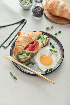 Croissant sandwich with cream cheese, cucumber and ham, served with a fried egg