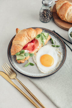 Croissant sandwich with cream cheese, cucumber and ham, served with a fried egg