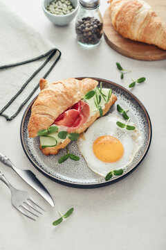Croissant sandwich with cream cheese, cucumber and ham, served with a fried egg