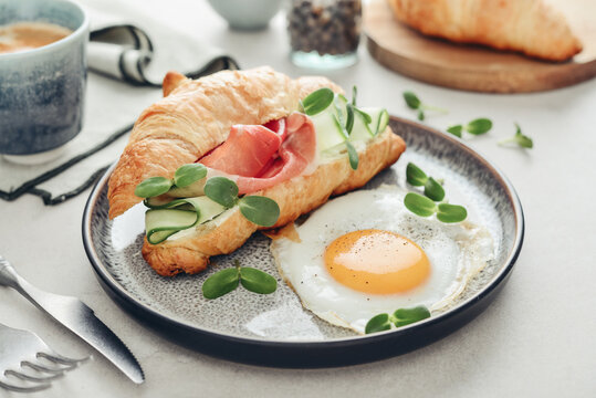 Croissant sandwich with cream cheese, cucumber and ham, served with a fried egg