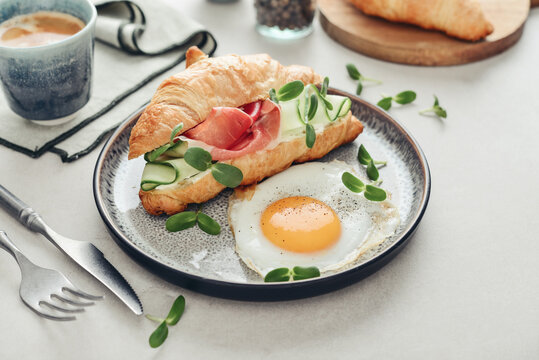 Croissant sandwich with cream cheese, cucumber and ham, served with a fried egg