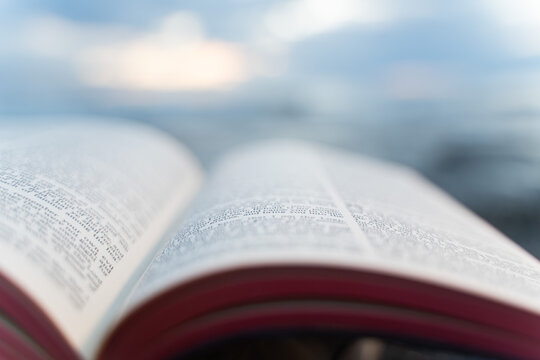Open Bible Book with Fluttering Pages on Rocky Beach at Sunset