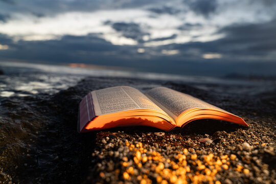 Open Bible Book Lying on Rocky Shore Against Moody Evening Sky 