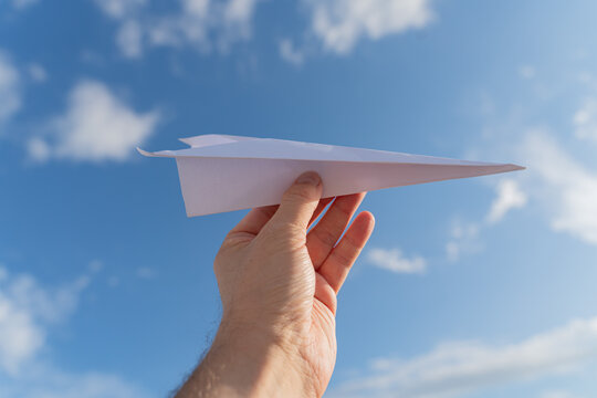 Hand Holding Paper Airplane Against Blue Sky with Clouds