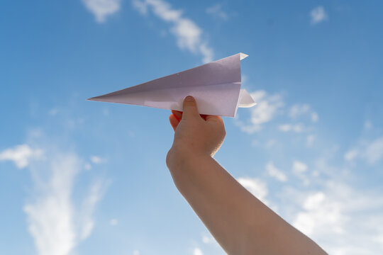 Hand Holding Paper Airplane Against Blue Sky with Clouds