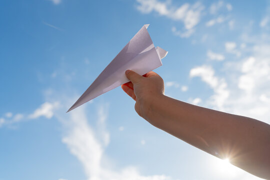 Hand Holding Paper Airplane Against Blue Sky with Clouds