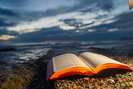 Open Bible Book Lying on Rocky Shore Against Moody Evening Sky 