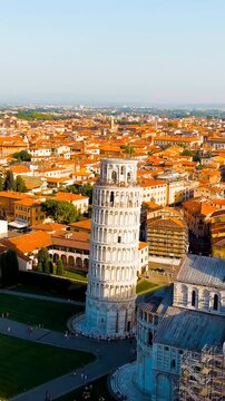 Vertical video. Pisa, Italy. The Leaning Tower and Pisa Cathedral in Piazza dei Miracoli, aerial drone view over the marble complex and terracotta rooftops at summer evening light. Drone footage. Ric