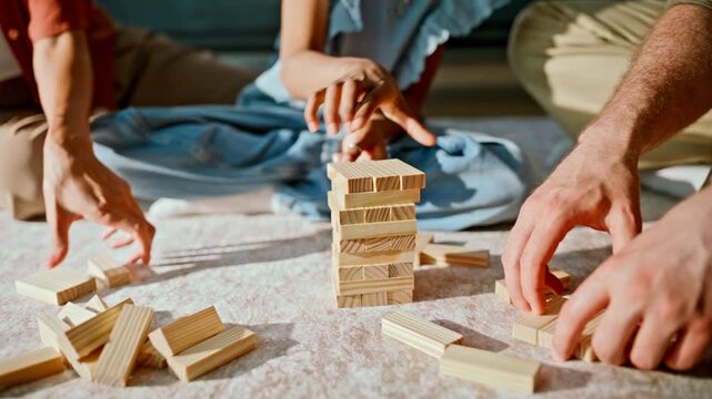 Multiracial parents daughter playing wooden blocks tower. Close up kid hands.