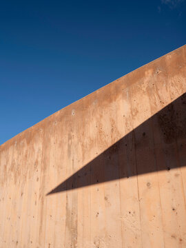 Close-up view of an angled adobe wall of a residential building in Santa Fe, casting a sharp triangular shadow across its adobe surface.