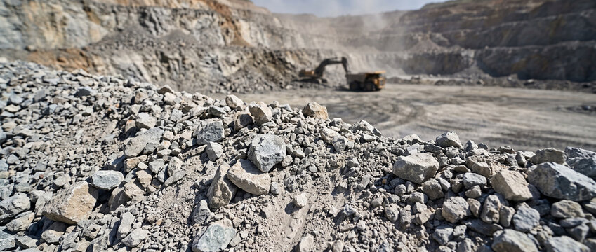 Rock quarry with excavator and haul truck at work in open pit. Stone extraction and aggregate production. Mining industry and earthmoving equipment. Construction materials.