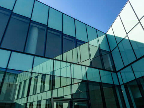Exterior view of a business office building's glass curtain wall facade, with angled sections meeting at a sharp diagonal line against the sky. 