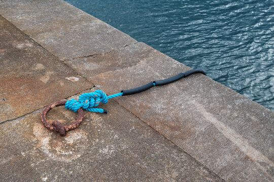 Blue mooring rope secured to a rusted metal ring on the concrete quay wall at the harbour in Hopeman, Moray, Scotland on a bright sunny day