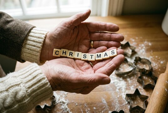Elderly hands cradling CHRISTMAS letter tiles beside star cookie cutters, symbol of tradition