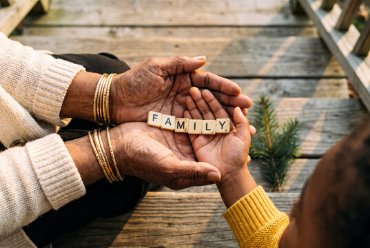 Elder hands with gold bangles and child hand holding FAMILY letter tiles, symbol of generations