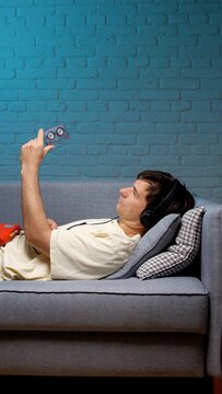Man lying on a sofa, wearing headphones and holding a cassette tape, reminiscing about the past and enjoying the retro music experience with old technology