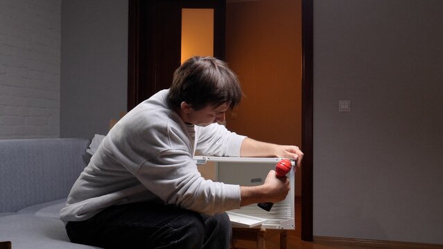 Man focusing on home improvement project, assembling new furniture with an electric screwdriver, working carefully on a do it yourself task in his apartment