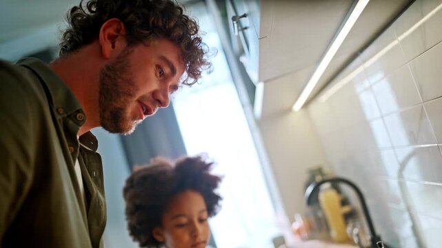 Smiling dad teaching daughter cooking omelette. Multiracial family home kitchen.