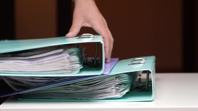 Hand opening a ring binder, organizing and archiving important business documents, paperwork, and financial records for office administration, legal, or educational purposes