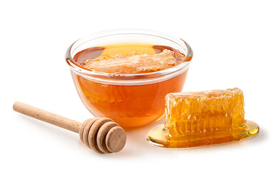 Studio shot of organic golden honey in glass bowl,  by afresh honeycomb piece and  wooden dipper. Isolated on white background for food and wellness concepts.