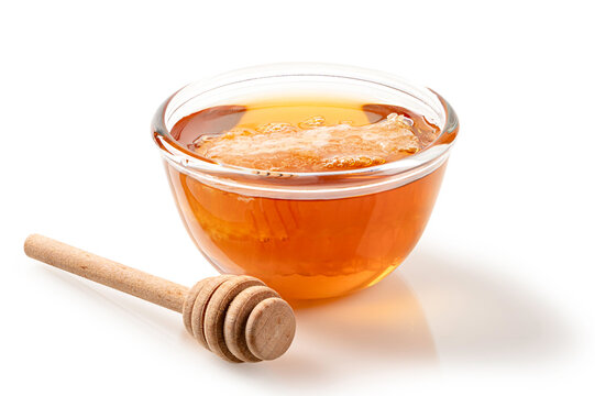 Organic golden honey in glass bowl with  fresh honeycomb slice and wooden dipper. Isolated on white background for food and wellness design.