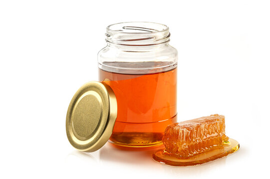 An open glass jar filled with organic golden honey, with fresh piece of honeycomb. High-quality product image for food branding and health concepts.