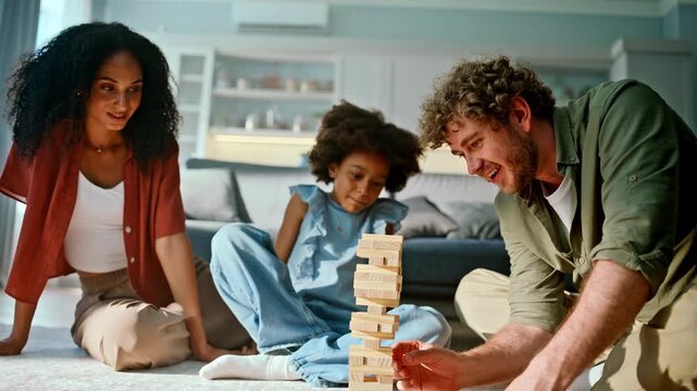 Daughter stacking wooden block tower parents. Happy family game living room.