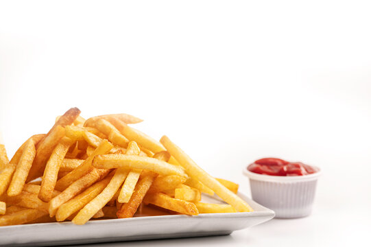 Delicious serving of hot, crispy golden french fries on a white square plate, served with a side of tomato ketchup. Professional food photography isolated on a white background.