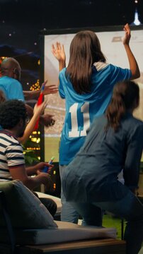 Vertical composition: Soccer supporters watch a projected match on a rooftop and discuss a controversial referee call, feeling worried during a tense nighttime sports event.