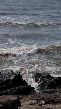 Waves Breaking Over Dark Coastal Rocks Along Gritty Shoreline in Gray Open Water