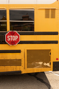 Yellow School Bus Side with Red Stop Sign. Close-up side view of a yellow school bus featuring a red octagonal stop sign, reflective windows, black protective strips.