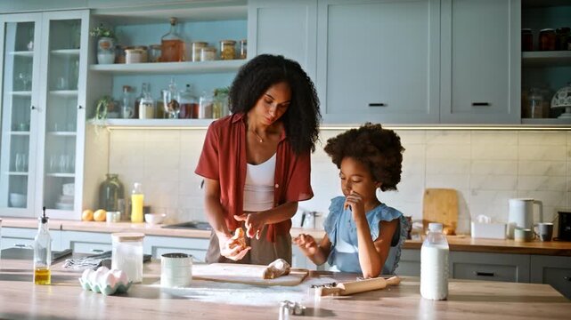 Girl helping mom shape dough kitchen. Multiethnic family baking together home.