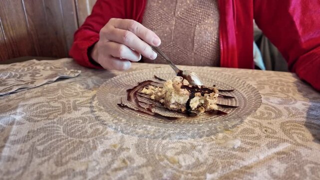 SLOW MOTION: Close-up of a woman eating cake dessert with chocolate. A tempting slice of layered cake, drizzled with chocolate, is being savored with a spoon in a restaurant of Italy
