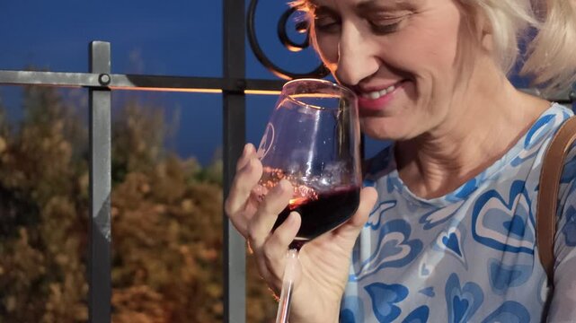 Blonde woman enjoying a sip of sparkling Lambrusco red wine from a glass during a wine festival in Castelvetro, Modena in Italy, focusing on the sensory experience of tasting.