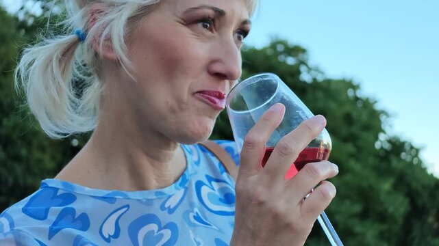 Blonde woman enjoying a glass of Lambrusco rose wine, participating in a wine festival in Castelvetro, Modena, Italy, focusing on the tasting experience in SLOW MOTION