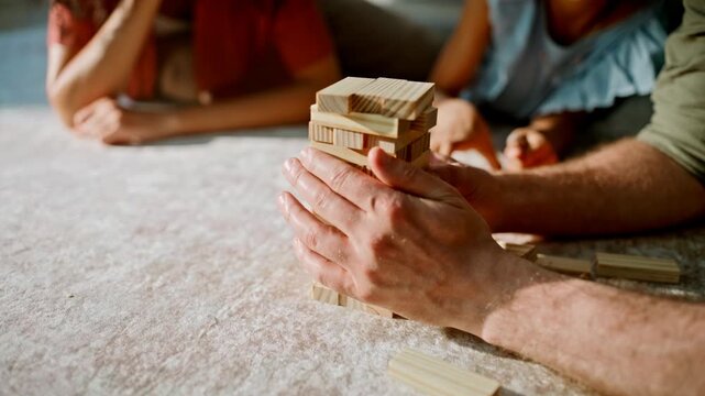 Family playing wooden block tower game home floor. Closeup hands, dad daughter