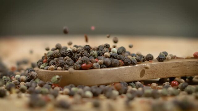 Mixed peppercorns falling onto wooden spoon close up in slow motion, preparing spices.
