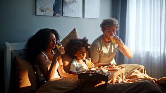 Parents daughter drinking orange juice bed. Morning breakfast tray cozy bedroom.
