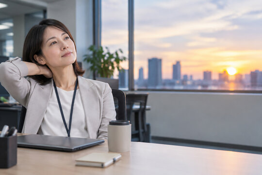 夕暮れのオフィスで首の後ろに手を添える女性