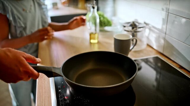 Girl pouring olive oil frying pan. Father holds pan handle modern home kitchen.