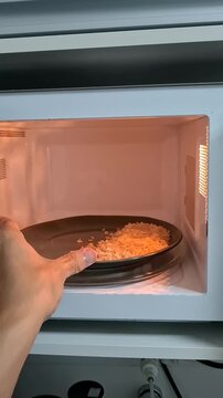 Person placing cooked rice in microwave for reheating at home, everyday meal preparation and convenient kitchen routine