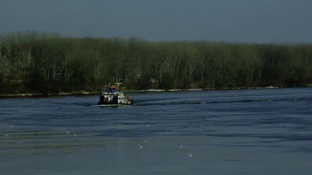 Tugboat navigating a wide river with forested shoreline under overcast, ocean