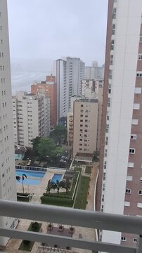 Rainy day view from apartment balcony window overlooking urban residential buildings, cloudy sky and wet city atmosphere