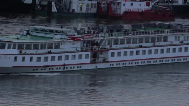 White river cruise ship STEAUA DUNARII cruising on calm waters at dusk with passengers on upper deck and docked vessels in background