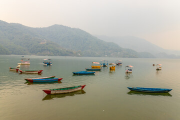 Colorful wooden boats floating on the calm waters of Phewa Lake in Pokhara, Nepal, surrounded by lush green hills and the dramatic Himalayan landscape of the Annapurna region © Yuliia