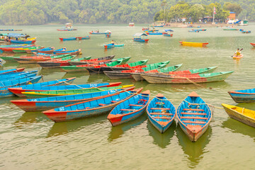 Colorful wooden boats floating on the calm waters of Phewa Lake in Pokhara, Nepal, surrounded by lush green hills and the dramatic Himalayan landscape of the Annapurna region © Yuliia